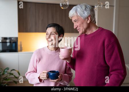 Coppia sposata anziana felice e ottimista, marito e moglie, che bevono caffè e conversano insieme a casa Foto Stock