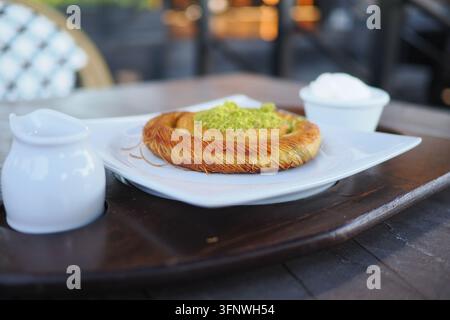 Pasticcino Kunafa caldo con pistacchio e panna servito su un piatto bianco in caffetteria Foto Stock