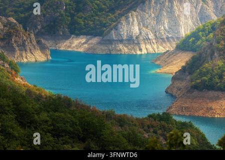 Vista aerea panoramica del lago Piva in Montenegro, circondato da montagne boscose impervie e acqua turchese, catturata da un punto di vista elevato nella morbida foschia mattutina Foto Stock