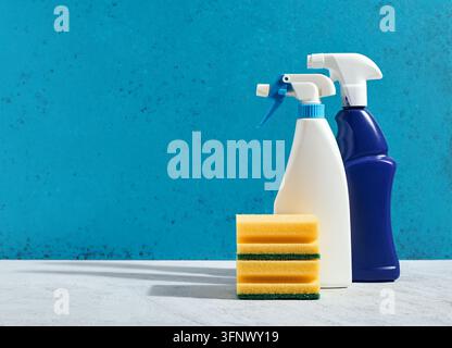 Bottiglie di spray per la pulizia e spugne gialle sul tavolo contro uno sfondo blu. Pulizia domestica, igiene, forniture per l'igiene e disinfezione delle superfici con Foto Stock