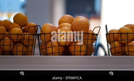 Arance fresche disposte in cesti di filo nero su un bancone di mercato. La composizione minimalista evidenzia colori naturali vibranti e una presentazione moderna e pulita Foto Stock