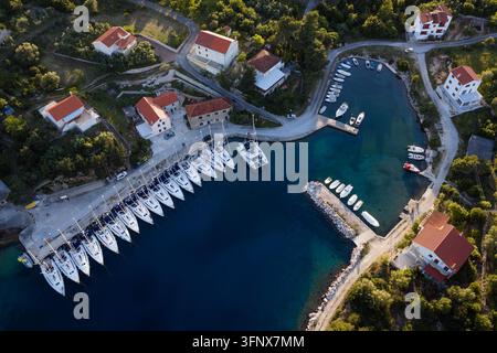 Veduta aerea dall'alto di un piccolo porto costiero con una fila di barche a vela e case tradizionali al tramonto Foto Stock
