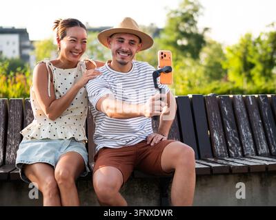 Uomo e donna sorridenti che registrano un vlog divertente insieme in un parco soleggiato. Foto Stock