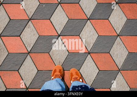 Gombak, Malesia – 18 maggio 2026: Scarpe da ginnastica arancioni vivaci su un pavimento a illusione ottica geometrica 3D Foto Stock