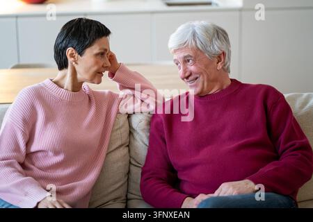 Coppia di anziani felici e attenti in una conversazione positiva mentre si rilassano insieme sul divano a casa. Foto Stock