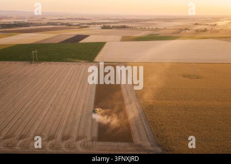 Una vista aerea cattura un raccoglitore verde che lavora efficientemente attraverso un vasto campo di soia. La macchina sta raccogliendo attivamente la soia matura Foto Stock