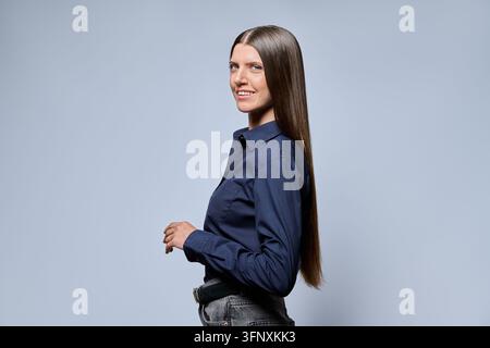 Giovane donna d'affari sicura di sé che sorride, in posa con una camicia smart casual su uno sfondo grigio da studio Foto Stock
