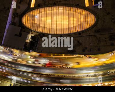 Vista aerea della struttura del tetto ovale illuminata sopra un'autostrada trafficata con scie di luce delle auto che passano di notte a Santo Domingo, Distrito Nacional Foto Stock