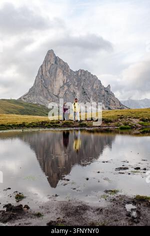 Due escursionisti vagano attraverso lo splendido scenario del Passo Giau nelle Dolomiti, Italia. I riflessi in uno stagno sereno esaltano il fascino pittoresco di Foto Stock