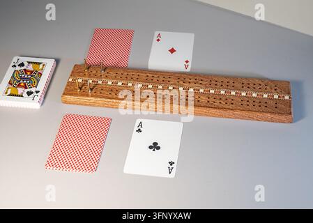 Tavola da cribbage in legno con pioli di metallo, un mazzo di carte, Asso di Quadri, Asso di Fiori e due carte coperte su una superficie grigia. Londra è visibile su Foto Stock