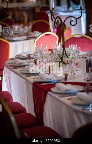 Primo piano di un tavolo da matrimonio con bicchieri a stelo, tovaglioli piegati, piatti bianchi e piccole fiale di vetro piene di bomboniere rosa, con petali di rosa Foto Stock