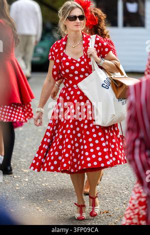 Partecipante attraente in abito a pois rossi e bianchi con borse della spesa al Goodwood Revival, con scarpe rosse abbinate e accessori d'epoca. Foto Stock