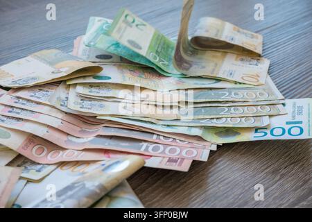 Varie banconote di dinaro serbo sparse su un tavolo di legno, che mostrano denominazioni colorate e banconote di carta piegate Foto Stock