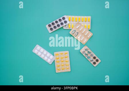 Diverse compresse, capsule e capsule morbide in confezioni a blister disposte su uno sfondo turchese con ampio spazio di copia circostante Foto Stock