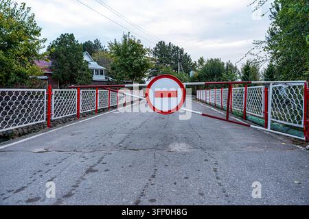 Barriera a scatto rossa e bianca con un cartello in mattoni che blocca l'accesso a una strada di villaggio rurale. Protezione della proprietà privata con un cancello chiuso Foto Stock