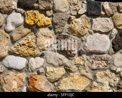 Primo piano di un muro di pietra rustico costruito con pietre naturali irregolari e malta consumata, che mostra una texture di muratura ruvida Foto Stock