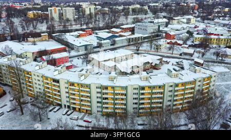 Vista aerea di un grande edificio residenziale curvo con facciata gialla e bianca circondato da strade residenziali innevate e da un edificio industriale Foto Stock