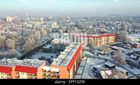 Vista aerea di una zona residenziale innevata con distintivi edifici residenziali dal tetto rosso circondati da alberi coperti di brina in Lettonia. Foto Stock