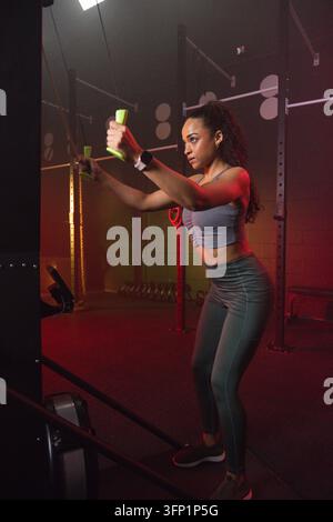 Donna afroamericana in abbigliamento sportivo che tiene maniglie verde brillante mentre esegue esercizi con cavo in palestra Foto Stock