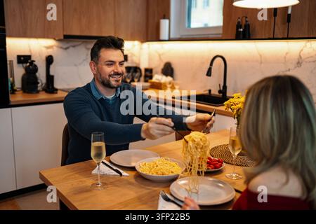 Uomo che serve della pasta a una donna durante una cena romantica a casa Foto Stock