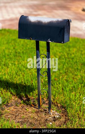 Cassetta delle poste residenziale nera su un palo metallico decorativo accanto a un prato verde in un quartiere suburbano, rappresentante la consegna della posta a domicilio e il servizio postale statunitense Foto Stock