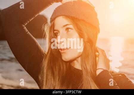 Donna, tramonto, ritratto di una giovane donna con un beanie all'aperto che si gode la calda luce dorata vicino all'acqua Foto Stock