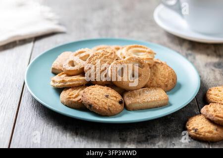 Vari biscotti al burro su un piatto con una tazza di caffè su un tavolo di legno Foto Stock