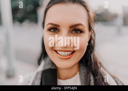 Donna ritratto sorridente di una giovane adulta con occhi marroni che indossa una sciarpa grigia alla luce naturale soffusa Foto Stock