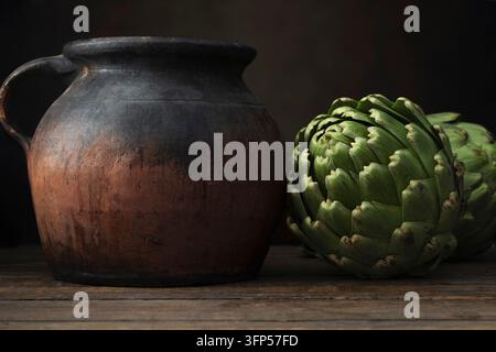 Due artischoki freschi e una ceramica rustica che striscia su una superficie di legno scuro Foto Stock