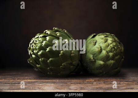 Due carciofi su superficie di legno scuro Foto Stock