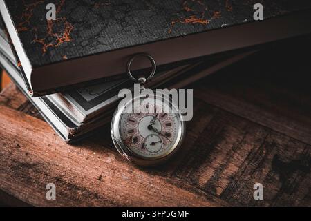 Vecchio orologio da tasca appoggiato contro una pila di libri Foto Stock