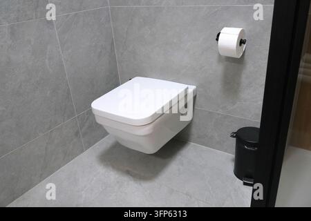 Toilette a muro con serbatoio integrato. Portarotolo e cestino nero. Bagno moderno generico di hotel in Polonia. Foto Stock