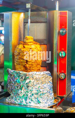 Un grande spiedo verticale di carne gira e griglia su una macchina per shawarma in un mercato di strada. Takeaway tradizionale mediorientale e asiatico fo Foto Stock