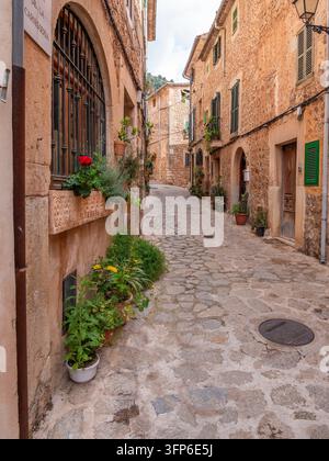 Valldemossa, Maiorca, una pittoresca e stretta strada acciottolata in una città storica fiancheggiata da edifici rustici, adornata con piante e fiori in vaso, exu Foto Stock