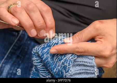 Una donna che lavora a maglia calzini colorati con un bel motivo alla luce naturale, primo piano delle mani Foto Stock