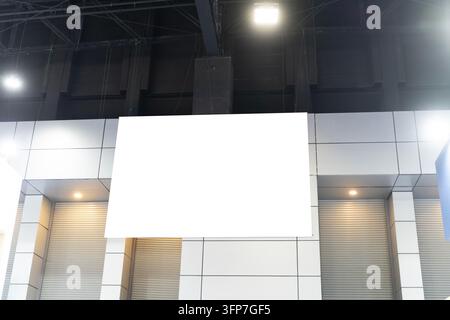 Grande schermo vuoto montato sulla facciata di un edificio moderno. Luci a soffitto brillanti illuminano la scena. Superficie bianca pulita pronta per i contenuti digitali. Perfetto Foto Stock