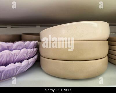 Una vista ravvicinata mette in mostra una pila ordinata di tre ciotole moderne in ceramica nei toni del beige e della crema, accanto a una pila di lavanda dal design intricato Foto Stock