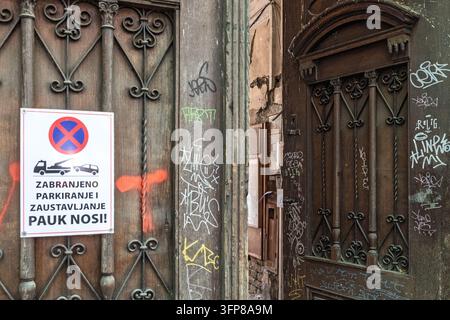 Un cartello su una porta coperta di graffiti avverte di non parcheggiare o fermarsi, affermando che i veicoli saranno rimorchiati, via Dimitrije Tucovića, Subotica Foto Stock
