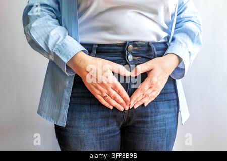 Donna che forma un cuore con le mani sopra l'addome in jeans per simboleggiare cura e salute Foto Stock