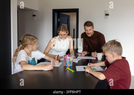 Famiglia felice con due bambini che giocano insieme a un gioco di disegno a casa. Tempo di qualità Foto Stock