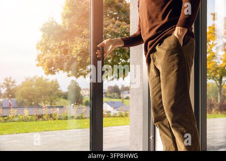 Uomo che apre una grande porta a vetri scorrevole in alluminio verso un giardino sul retro Foto Stock