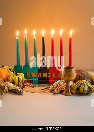 Kinara Kwanzaa con sette candele accese circondate da frutti tradizionali delle feste Foto Stock