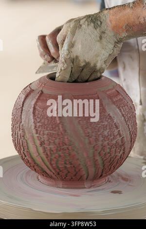 Mani artigiane che modellano e textureggiano un vaso di argilla rotante su un tornio da vasaio, primo piano della tradizione artigianale e del processo creativo tattile di Foto Stock