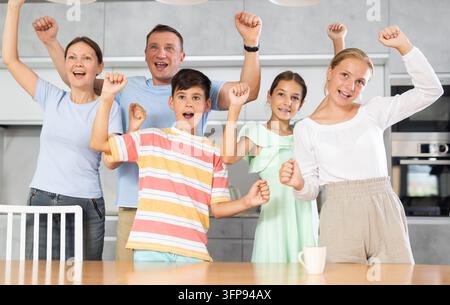 Una grande famiglia è felice dei cambiamenti positivi e delle buone notizie dall'istituto educativo dei bambini. Genitori che ridono e sorridono con i bambini sollevano Foto Stock