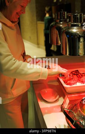 Ritratto verticale di una donna matura sorridente che usa delle pinze sotto una lampada termica durante un buffet cena in un ristorante di lusso di un resort. Foto Stock