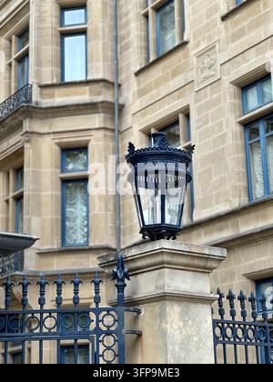 Lampada da strada vintage ornata e recinzione in ferro davanti a un edificio storico in pietra europea. Elegante lanterna vintage nera su un pilastro in pietra con una decorazione Foto Stock