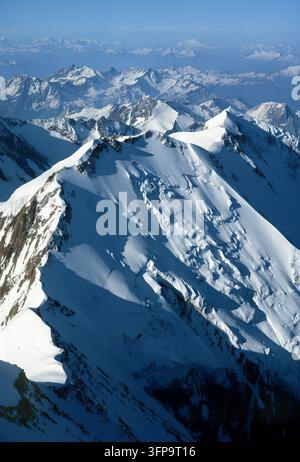 Una straordinaria prospettiva aerea mostra una vasta distesa di montagne innevate sotto un cielo azzurro limpido. Il terreno accidentato e le ombre drammatiche creano Foto Stock
