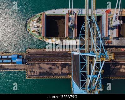 Vista aerea di una nave portacontainer caricata con carbone da una grande gru in un terminal portuale, con nastri trasportatori e infrastrutture industriali a Ci Foto Stock