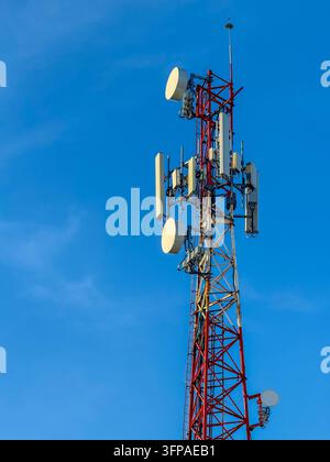 Alto traliccio di telecomunicazioni rosso e bianco con più antenne contro il cielo blu – Infrastruttura di rete mobile Foto Stock