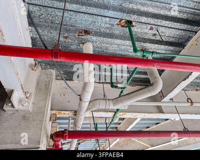 Tubi industriali colorati rosso verde bianco sotto soffitto in lamiera ondulata – Dettaglio dell’infrastruttura idraulica urbana Foto Stock